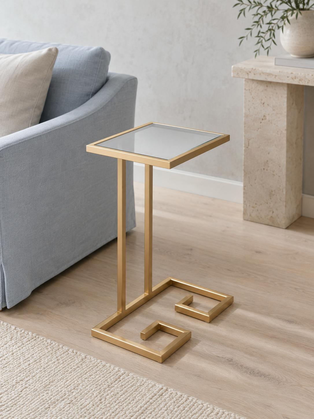 Meander PVD gold C-shaped corner table with square mirror-glass top beside a light blue sofa
