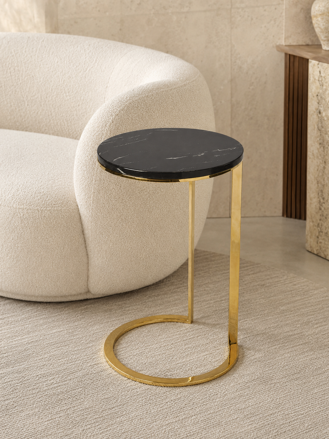 Eclipse PVD gold C-shaped corner table with round black marble top and circular base beside a cream sofa