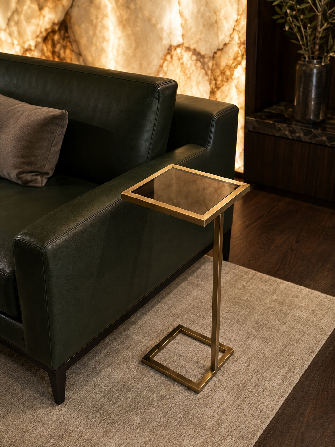 Axis PVD gold C-shaped corner table with square smoked mirror-glass top beside a dark green leather sofa