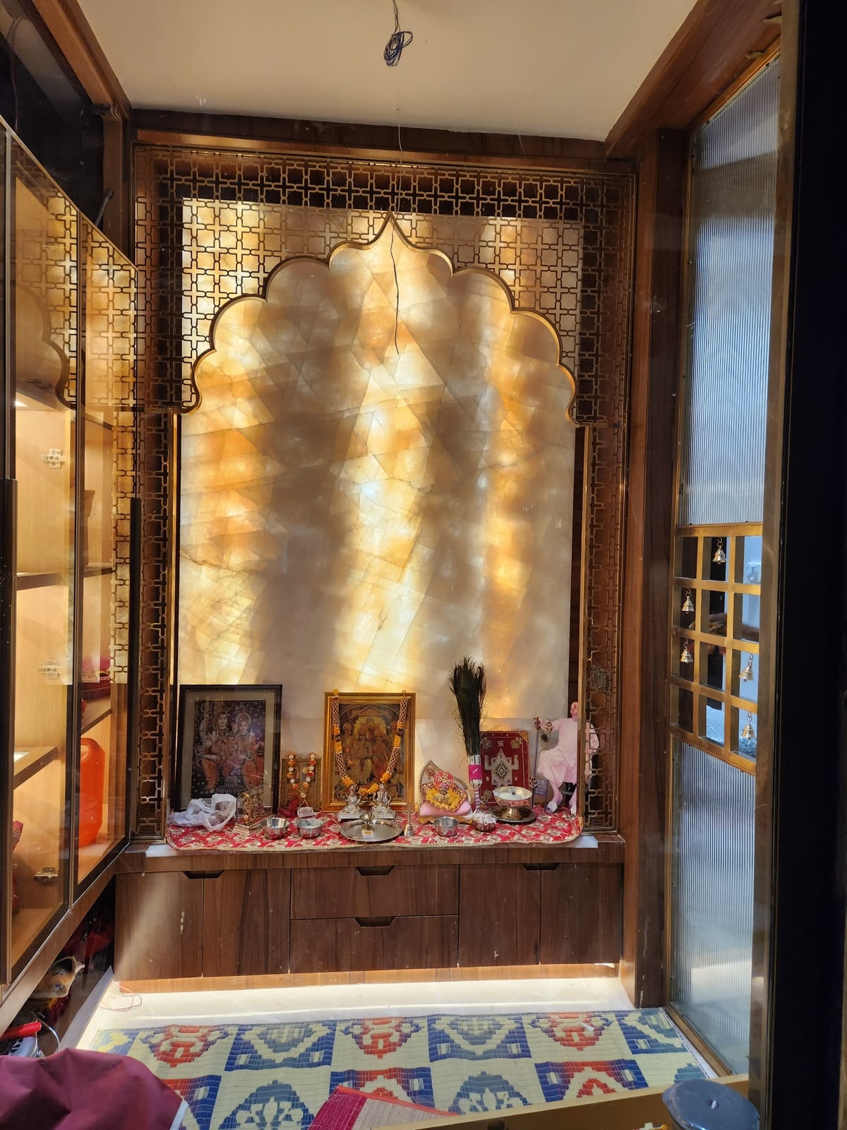 A custom-designed pooja room feature combining intricate gold metal jali work with an illuminated stone backdrop.