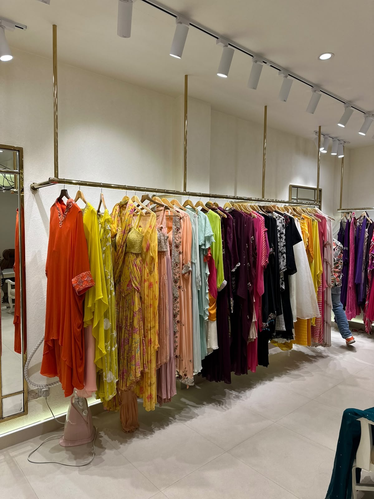 A minimal ceiling-suspended gold metal clothing rail designed for a premium fashion retail environment.